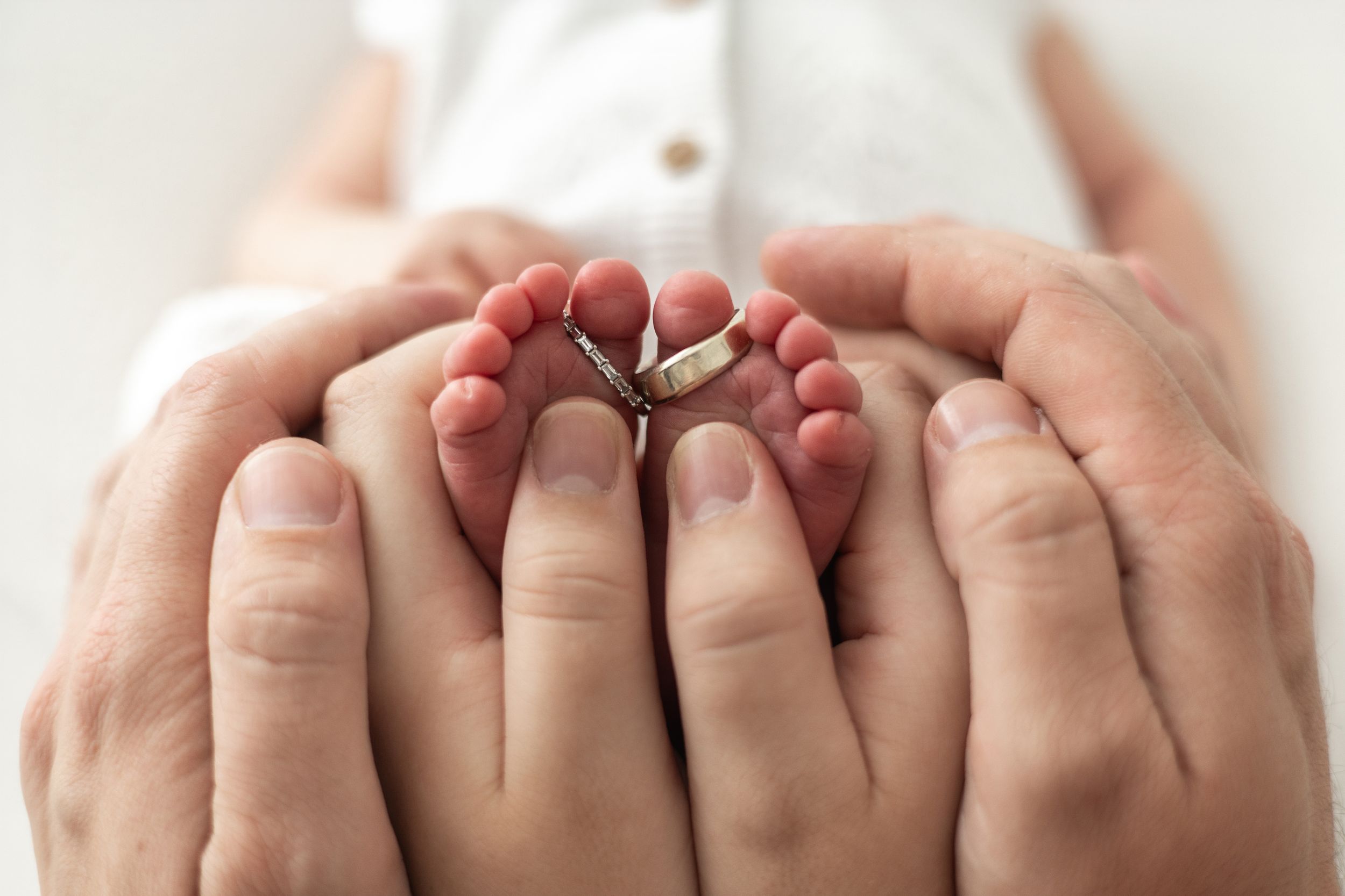 Parents hands cradling tiny newborn baby feet with wedding rings placed on the toes relaxed newborn photoshoot Nottingham