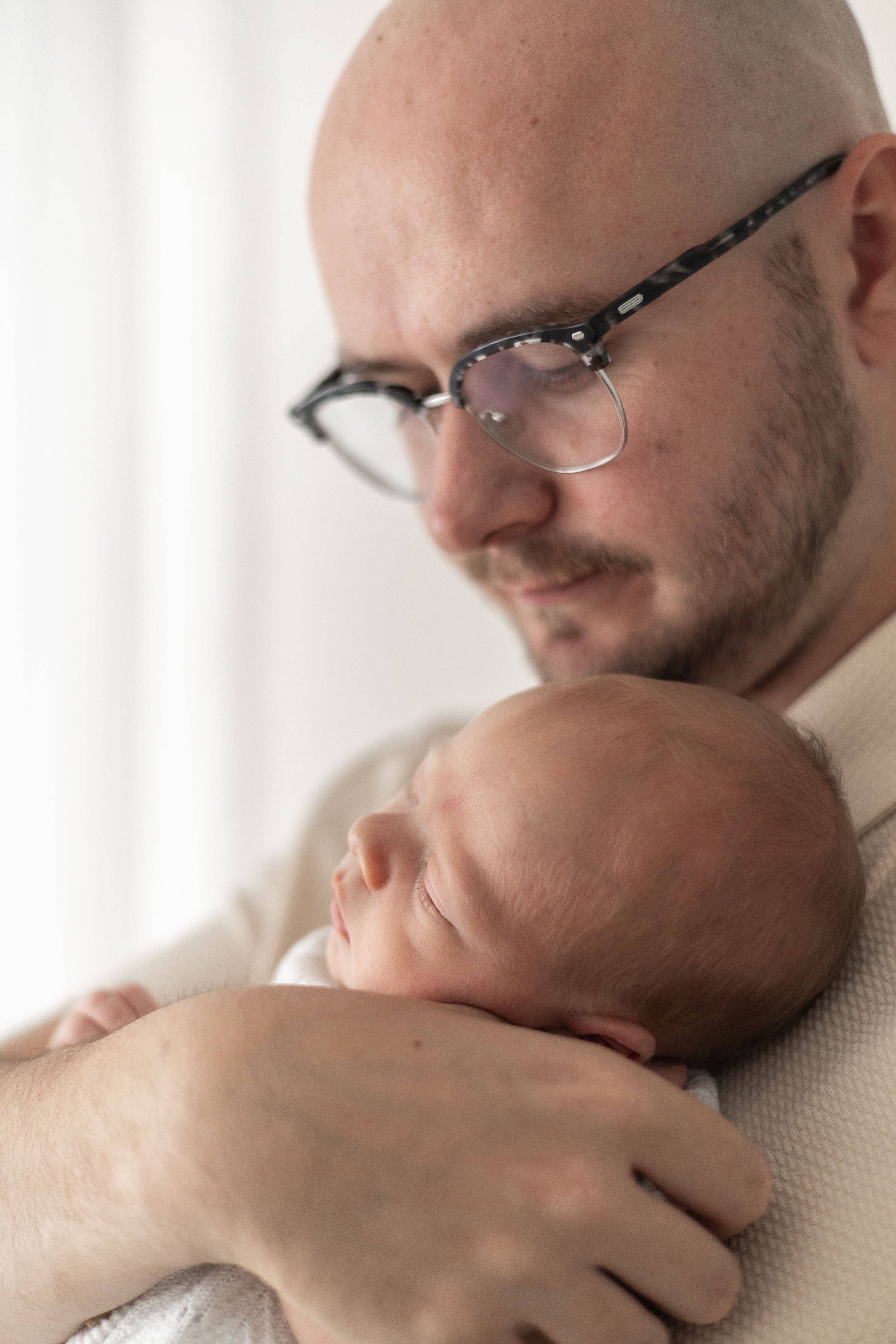 A Dad tenderly holds sleeping newborn baby close to his chest in soft natural light relaxed newborn photoshoot Nottingham