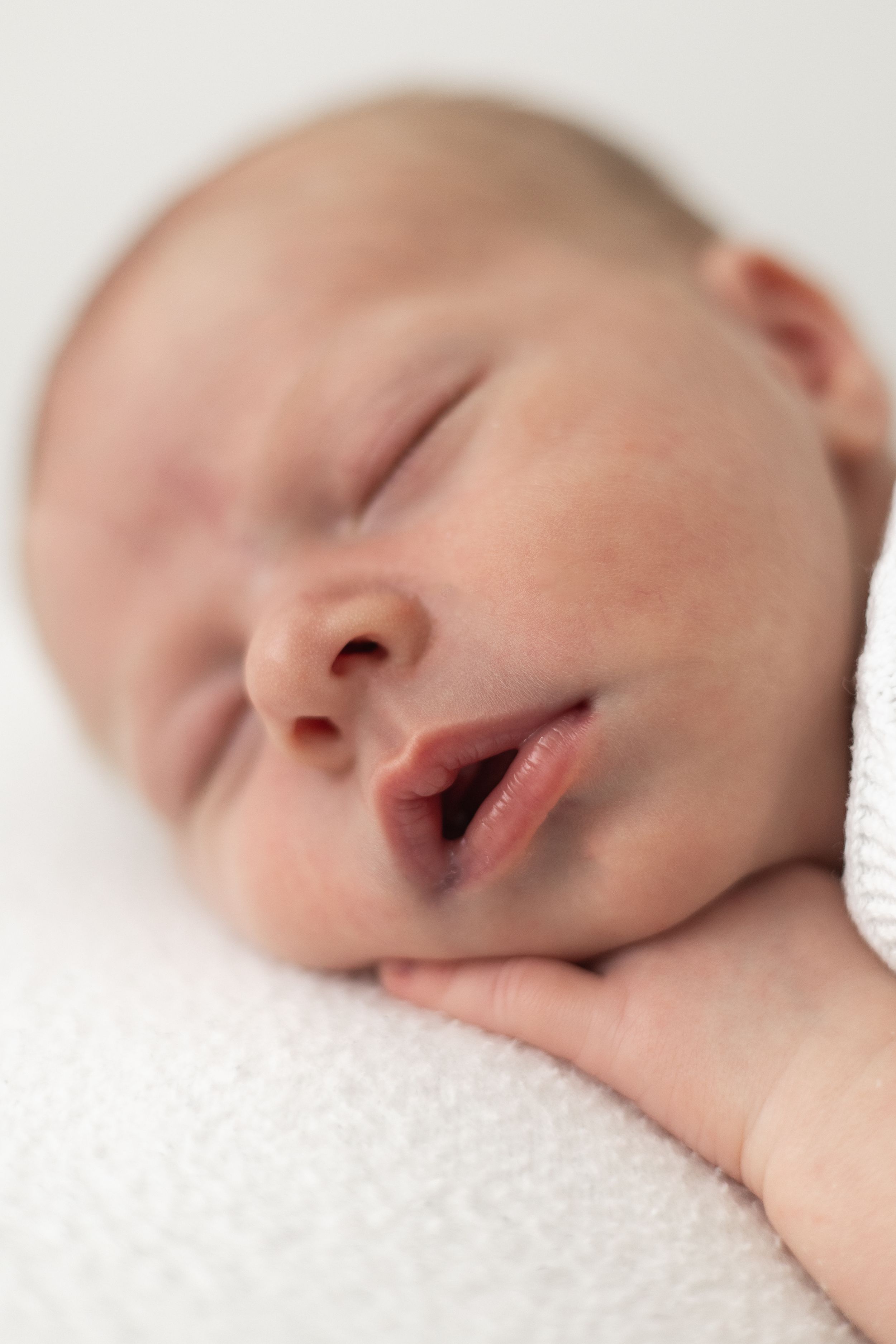 Peaceful newborn baby sleeping with mouth slightly open, resting on a soft white blanket relaxed newborn photoshoot Nottingham