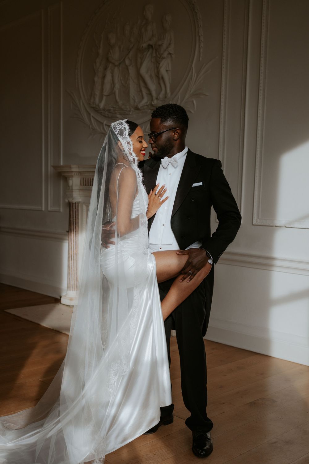 Bride in white gown and groom in tuxedo share intimate moment during indoor wedding photoshoot.