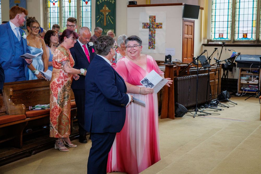 Wedding guests in colorful formal attire socializing inside a church decorated for a ceremony.