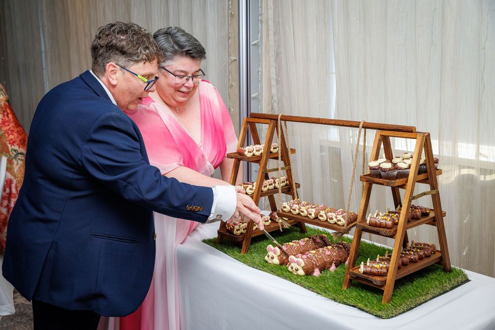 Couple cutting a tiered wooden dessert display at a formal celebration event.