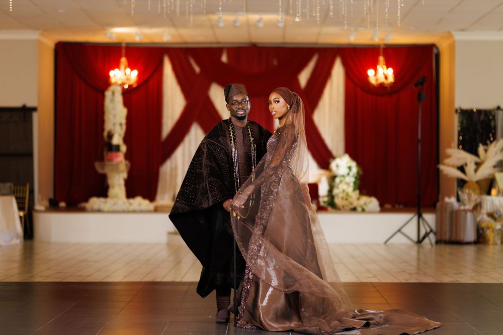 Elegant couple posing in wedding attire on a dance floor with red and white draped backdrop and chandeliers.