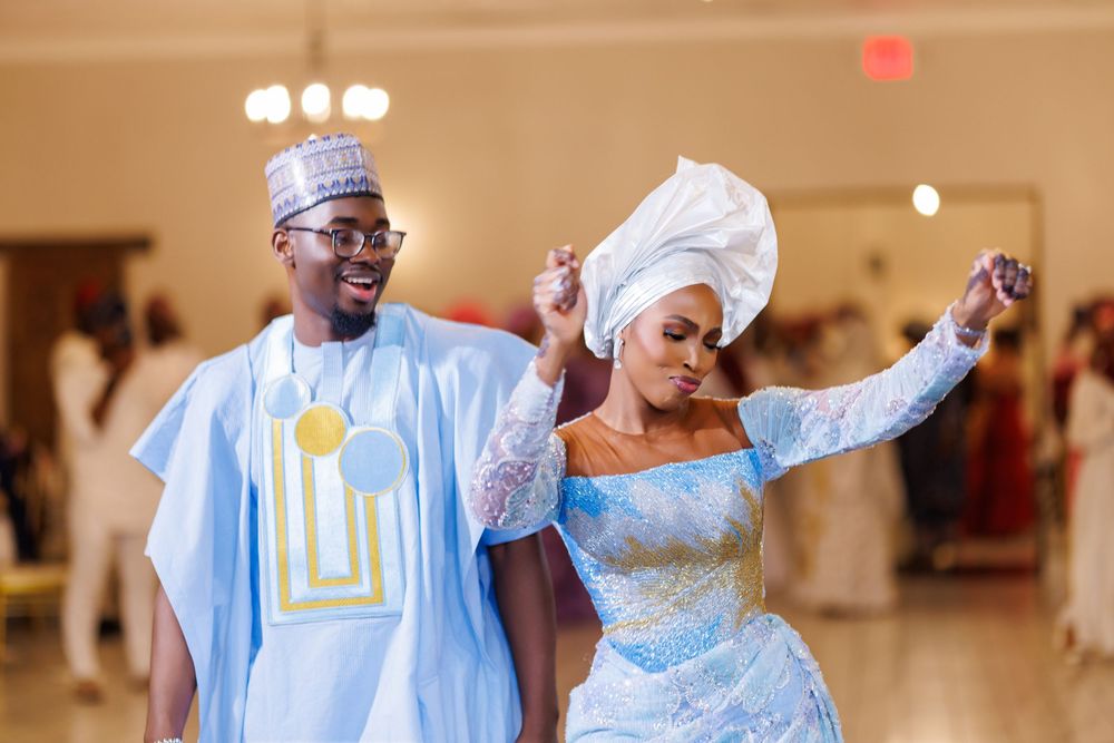 Couple in traditional Nigerian wedding attire dancing joyfully at a reception venue.