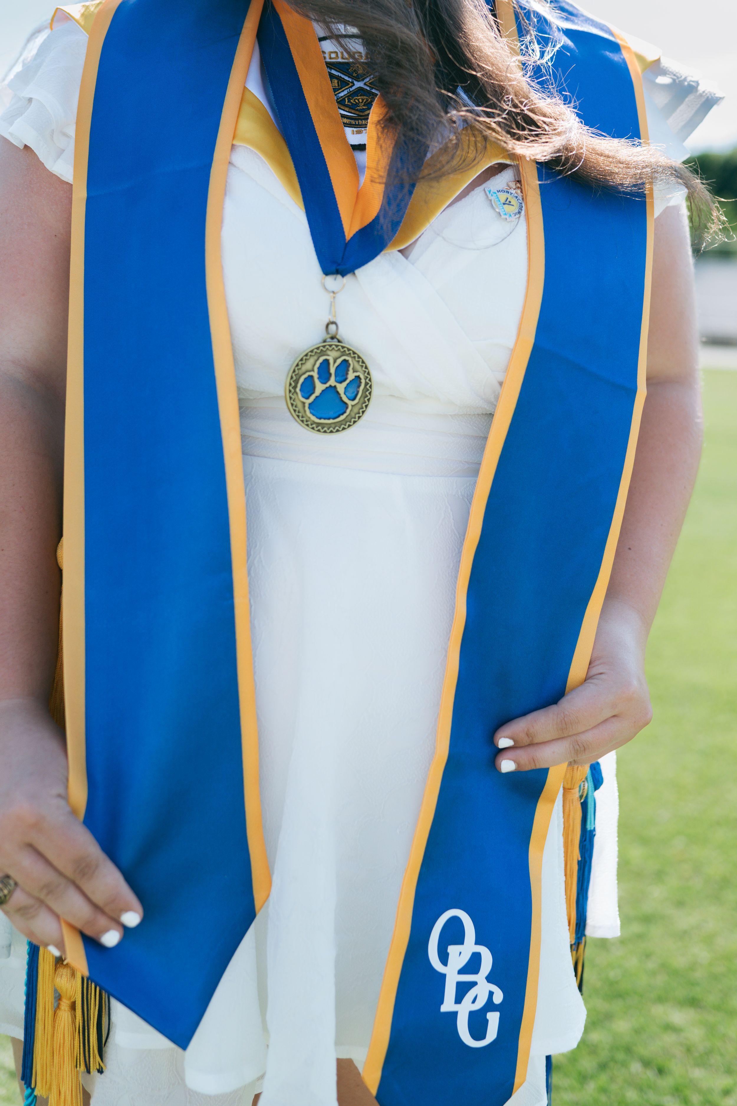 Close-up of graduate wearing blue and gold honor stole with paw print medallion at outdoor graduation ceremony, portrait photographer NC