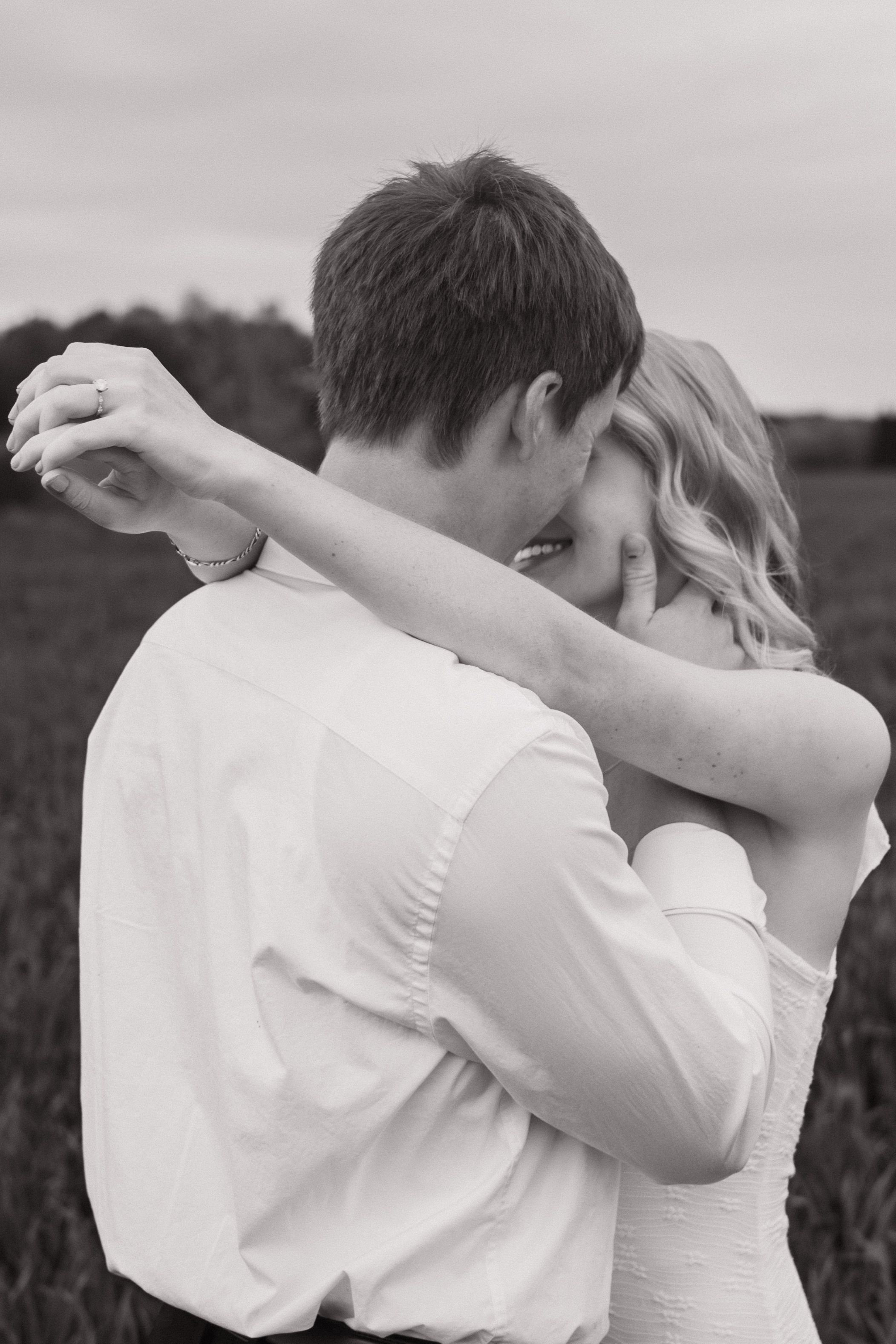 Black and white photo of a couple embracing romantically in an open field, engagement photographer Greensboro NC