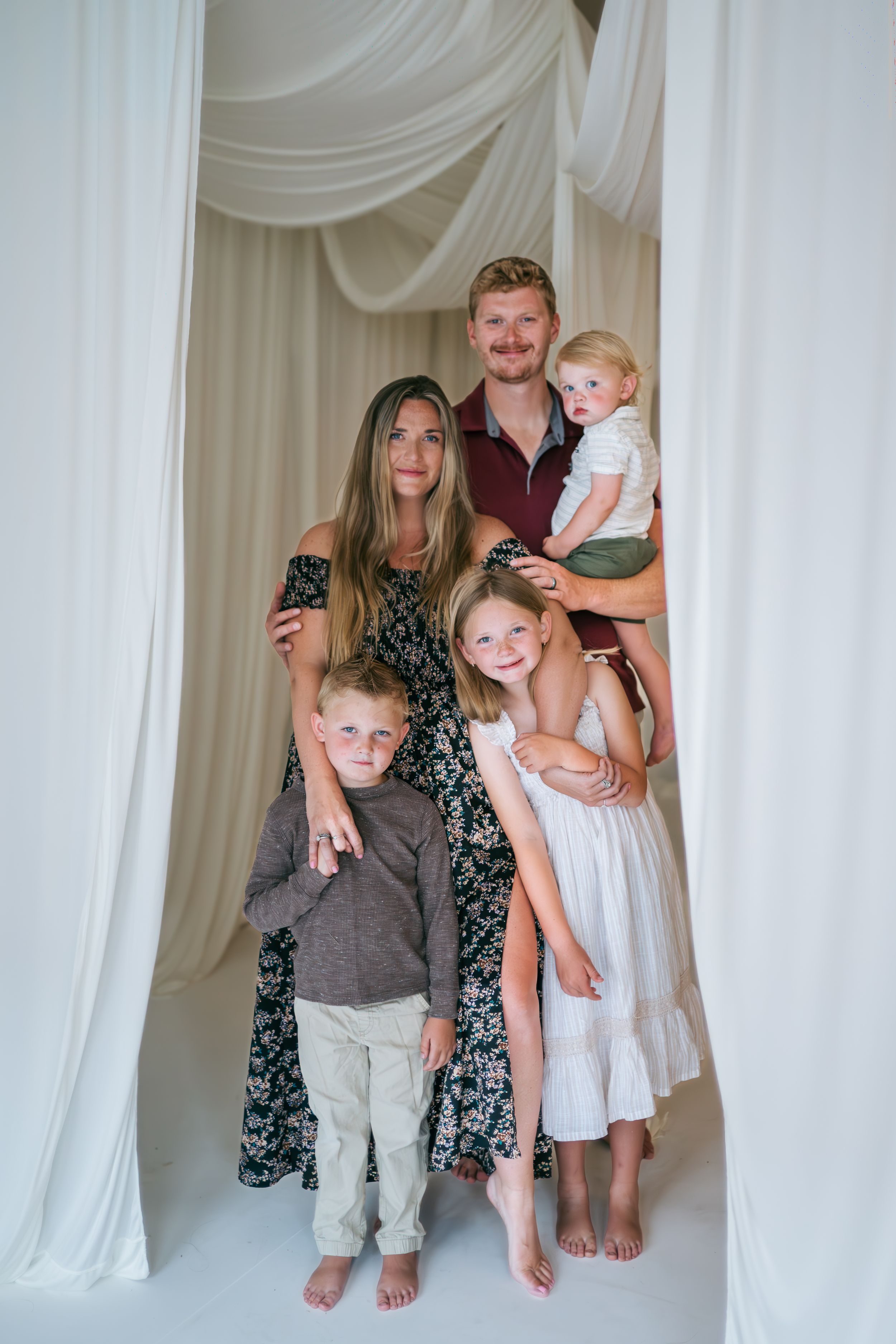 Family of five posing together between white draped curtains in bright studio, family photographer Lexington NC