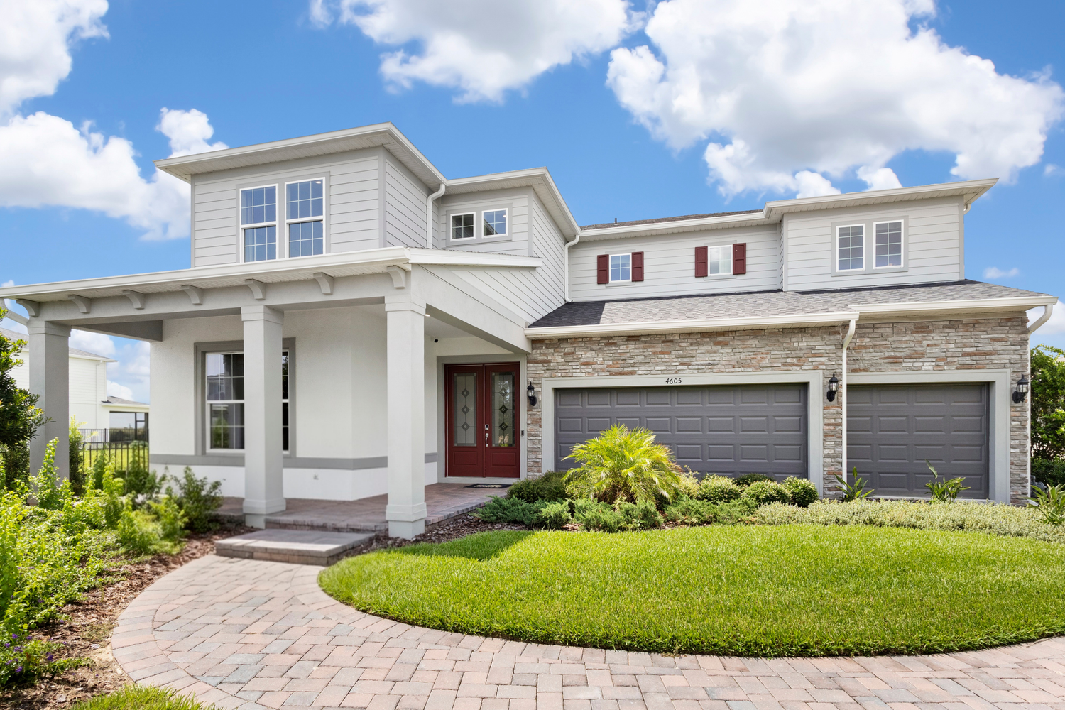 Modern single-story home with gray stucco exterior, blue front door, large windows, and lush green landscaping under a blue sky.
