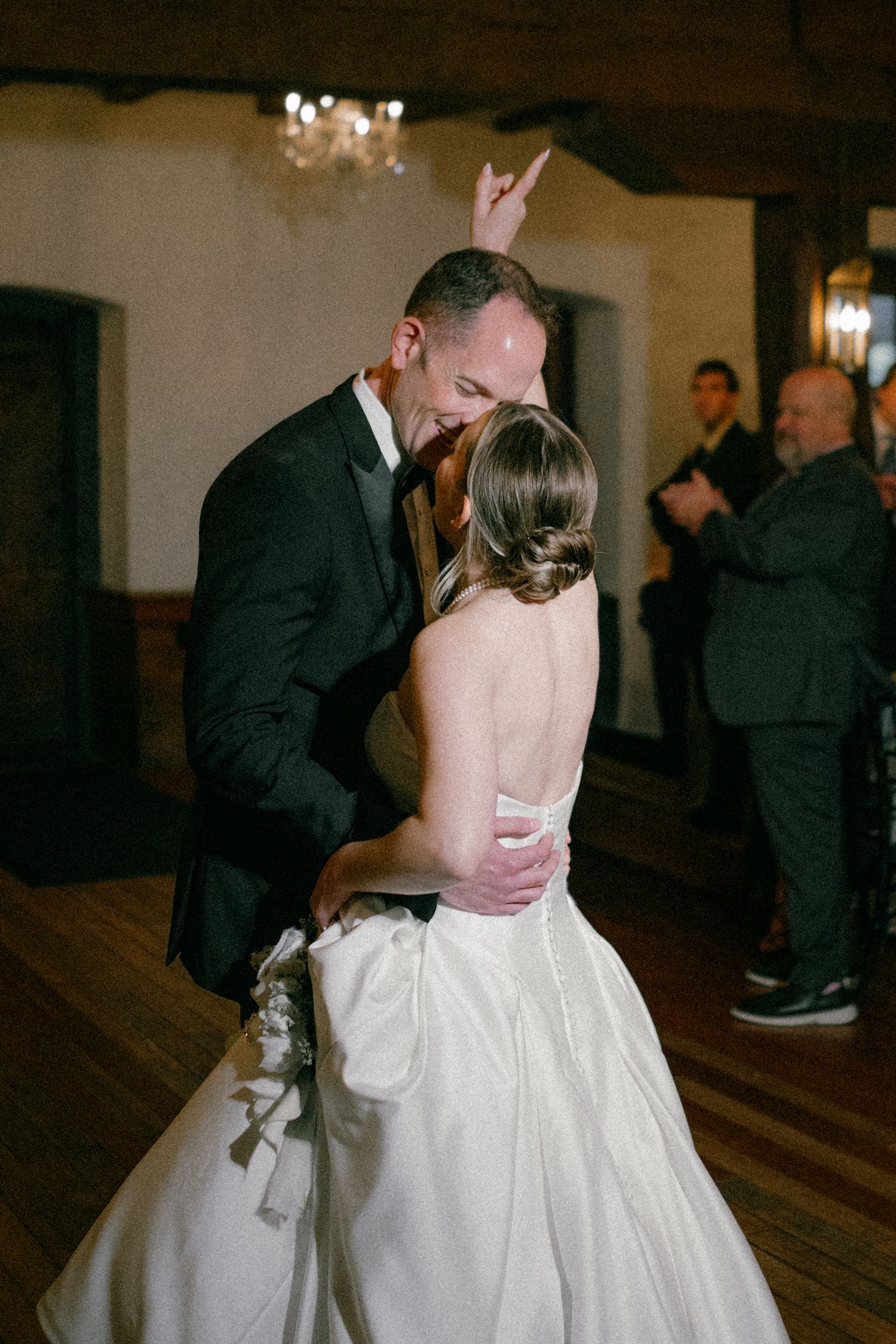 Groom in black tuxedo dips and kisses his bride in a white ball gown during their first dance.
