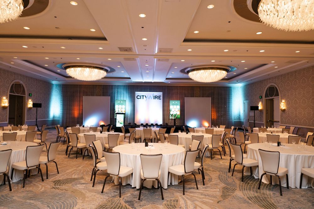 Elegant banquet hall with round tables, white linens, chandelier lighting, and a CityWire presentation screen at the front.