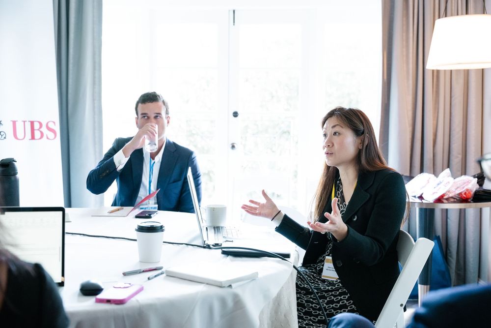 Two professionals in discussion at a UBS conference table, woman gesturing while speaking, man listening attentively.