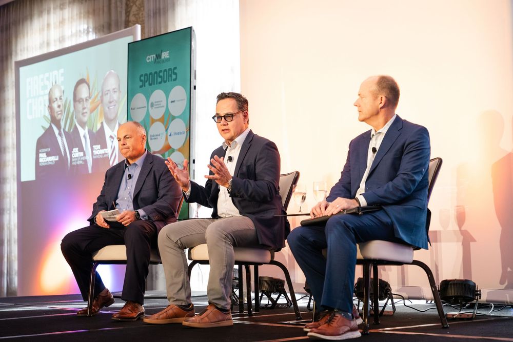 Three business professionals engaged in a panel discussion on stage at a corporate conference event.