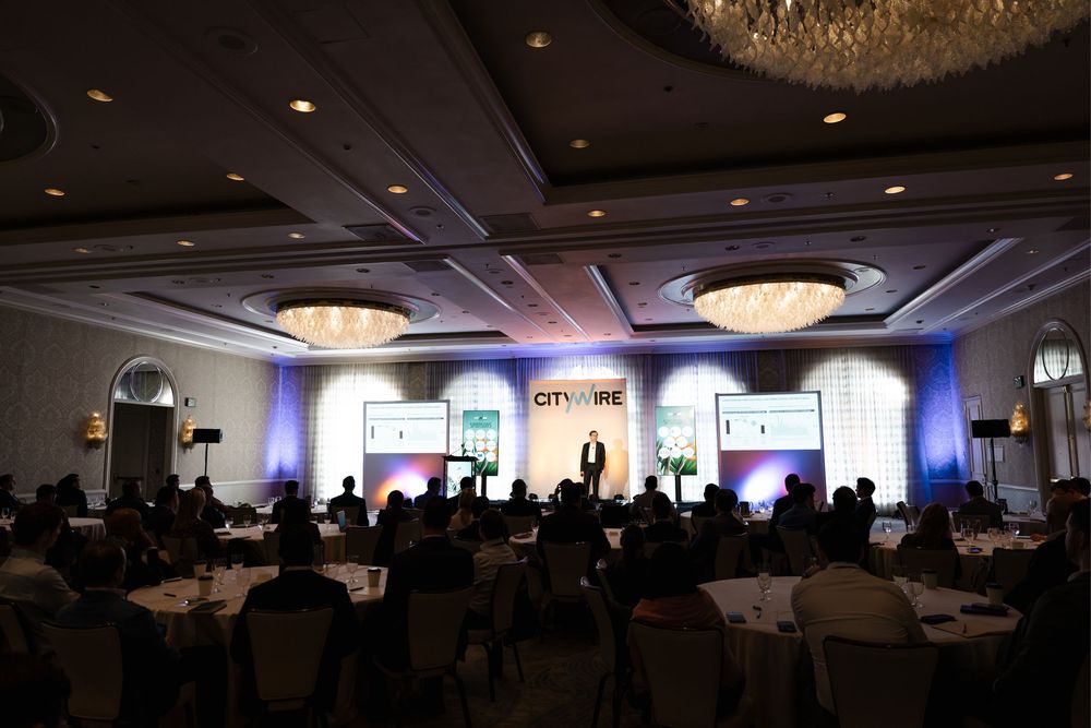 A large Citywire conference event in an elegant ballroom with chandeliers, round tables, and a speaker on stage.