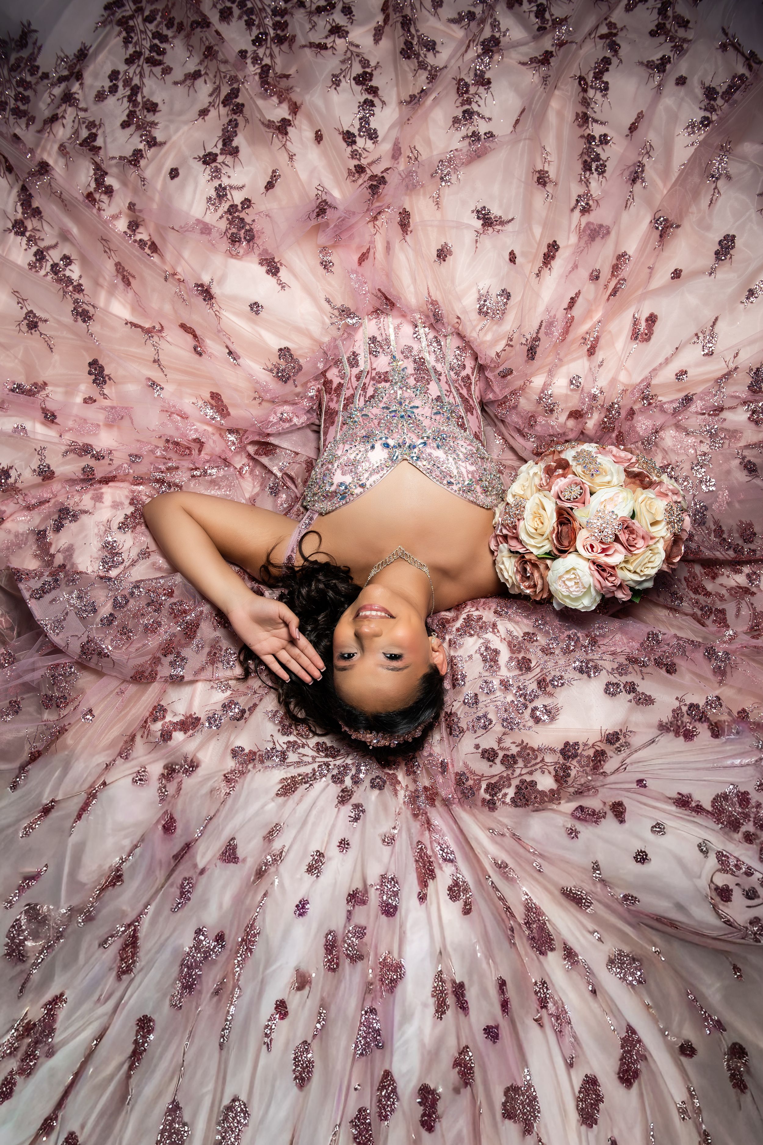 Young woman in a pink sequined ball gown lying on the floor holding a bouquet of roses.