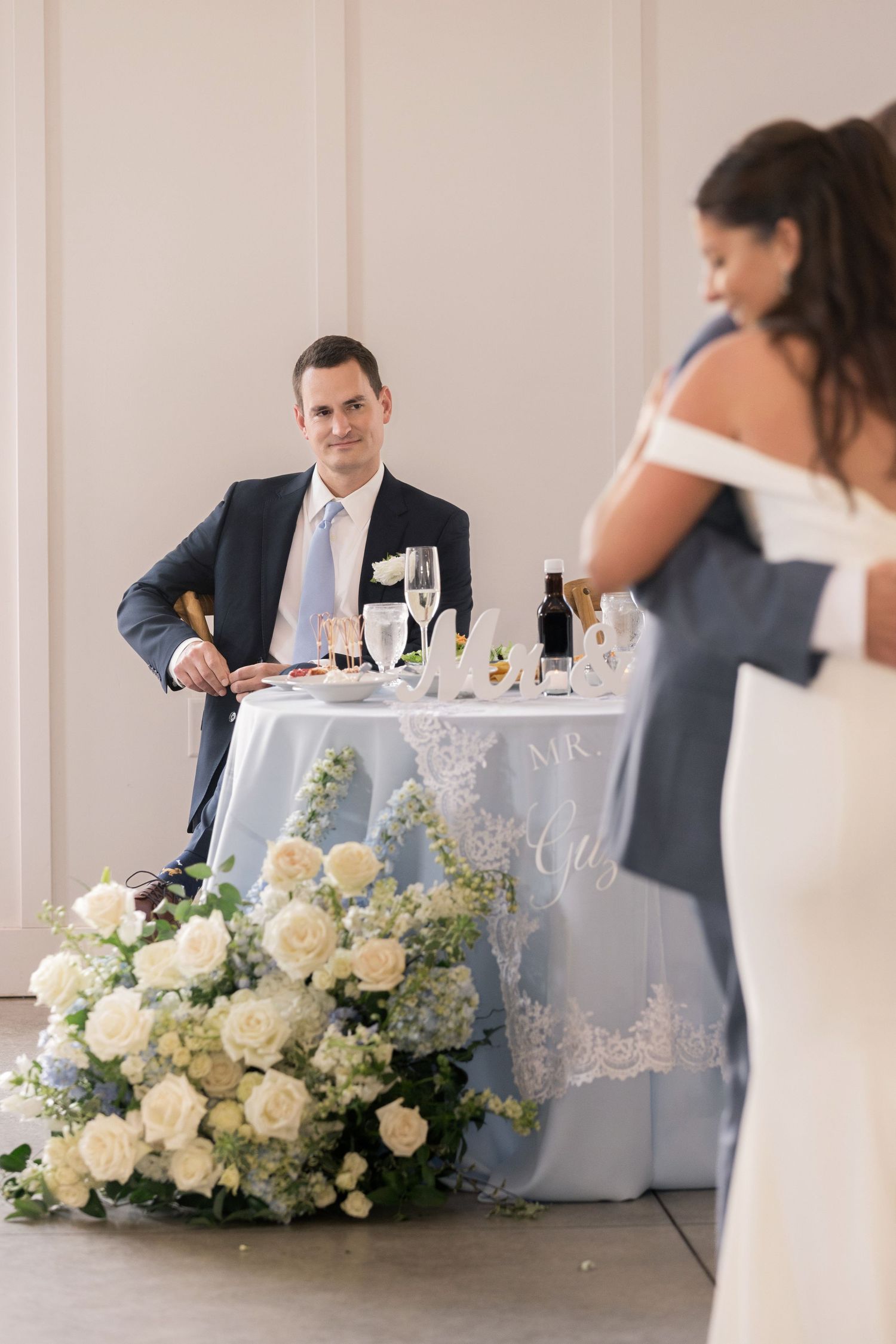 Elegant wedding reception in a white barn venue with string lights, guests seated at decorated tables.