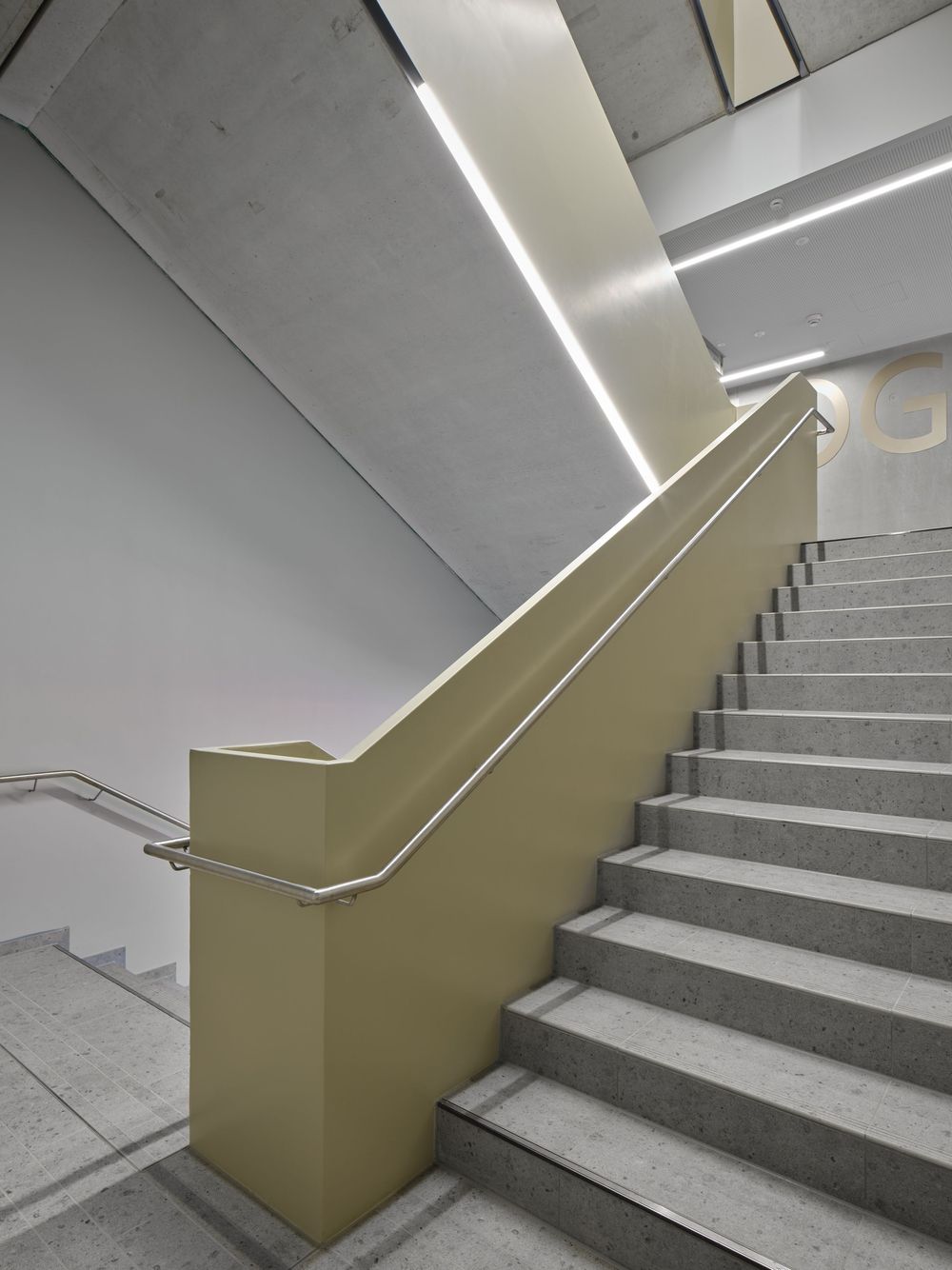 Modern concrete staircase with pale yellow railing wall, stainless steel handrail and recessed linear LED lighting in a minimalist interior.