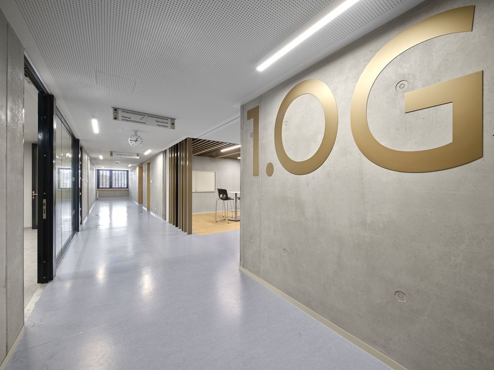 Modern office corridor with a polished floor and a large gold 1.0G floor number mounted on a gray concrete wall.