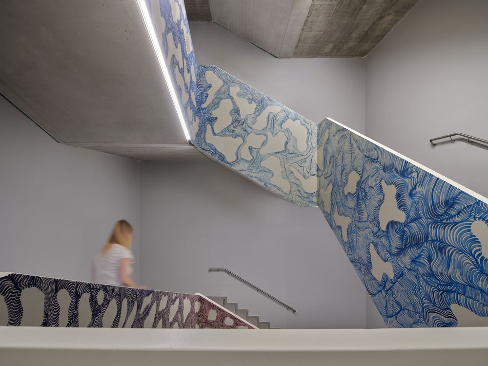 Woman walks past a modern concrete staircase with blue and white wave-patterned murals covering the angled walls and railings.