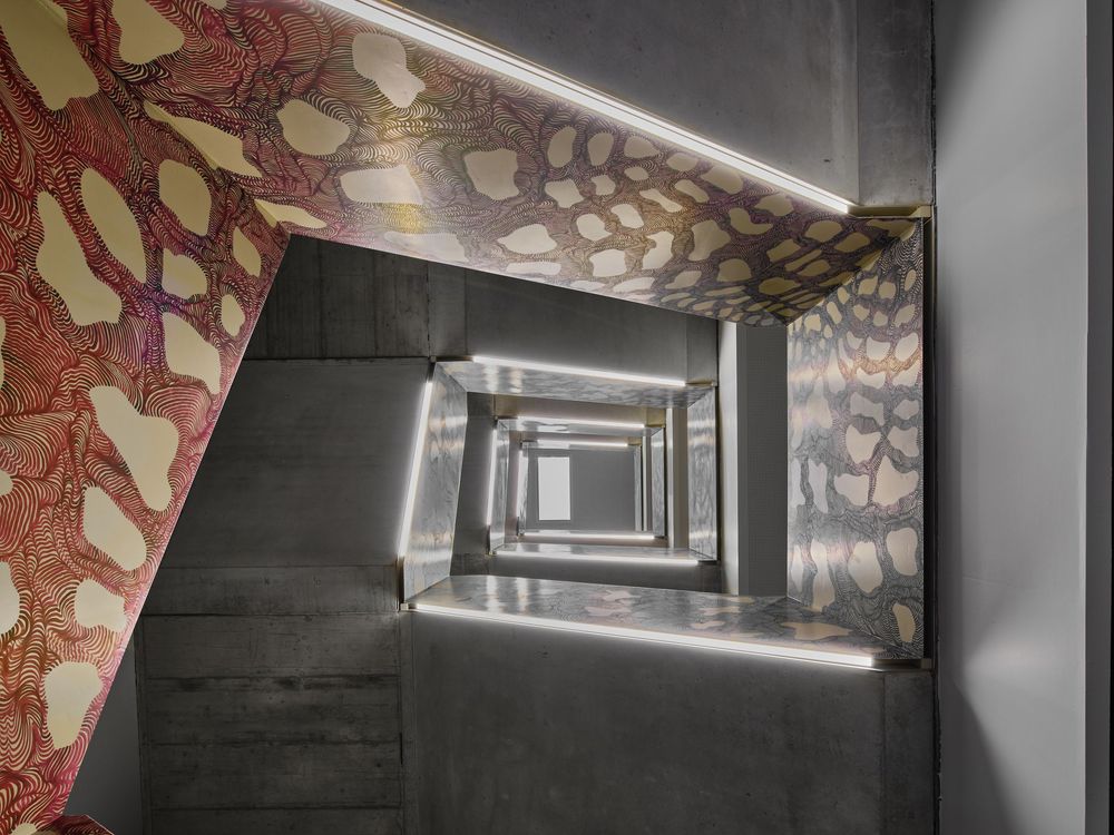 Looking down a modern concrete stairwell with sleek LED strip lighting and walls covered in an ornate red and cream organic pattern.