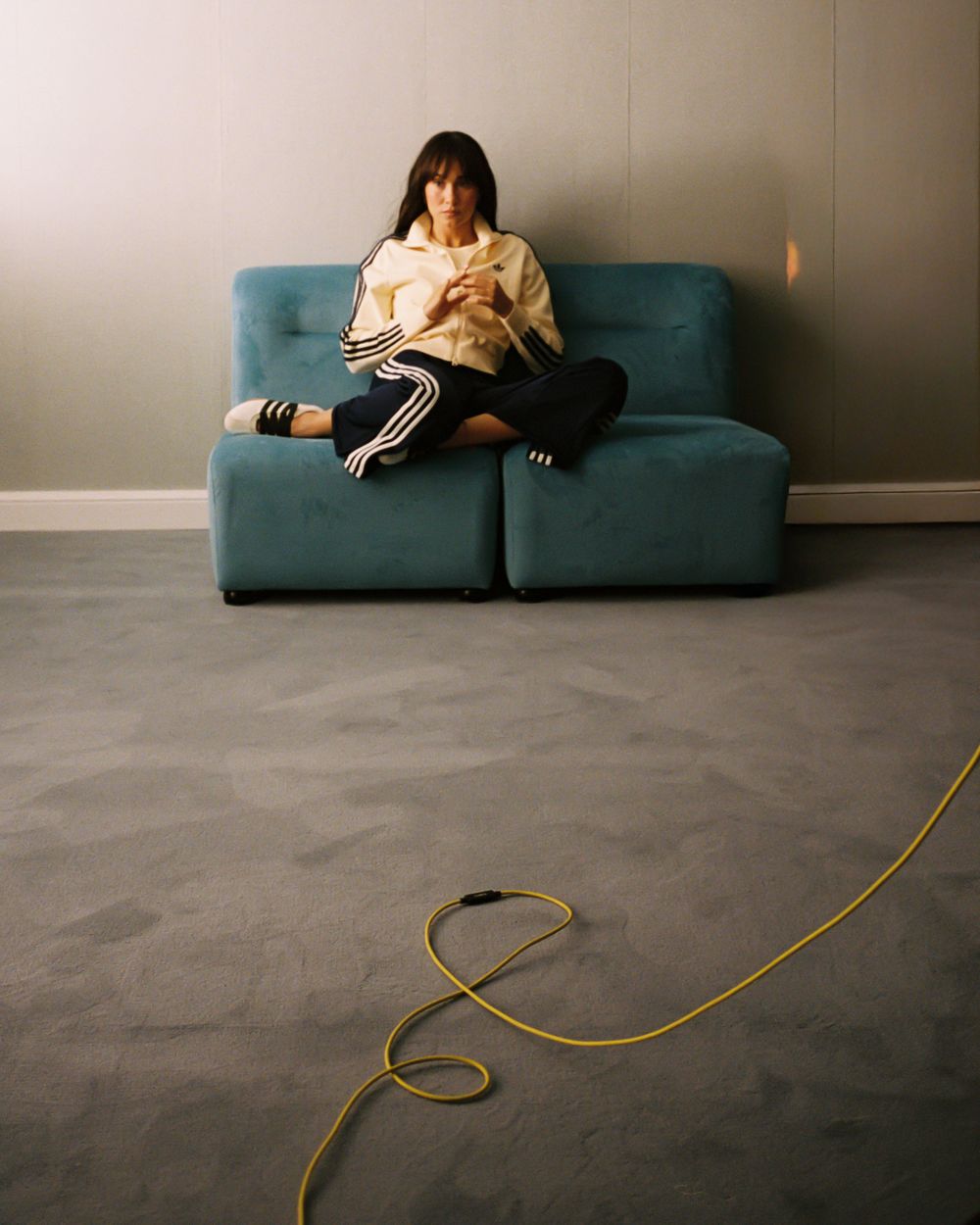 Person sitting cross-legged on a teal sofa using a phone, with a yellow cable on the floor nearby.