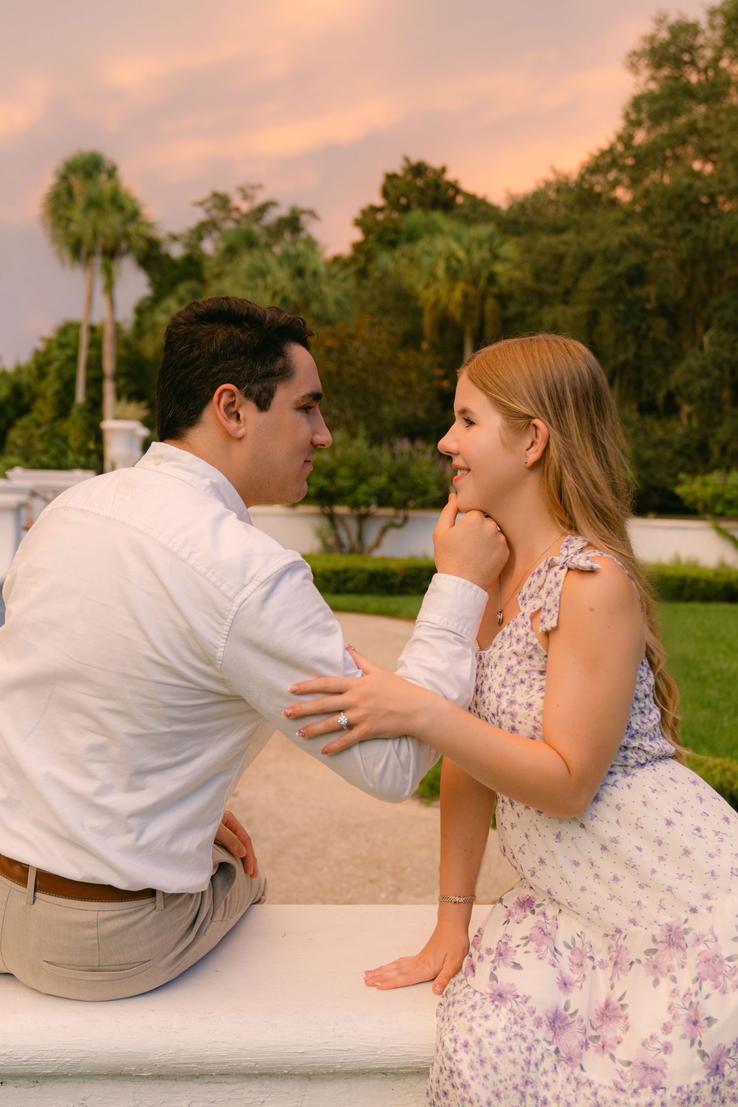 Engaged couple sharing a quiet moment beside a white garden wall beneath a colorful sunset sky in the Golden Isles, Georgia