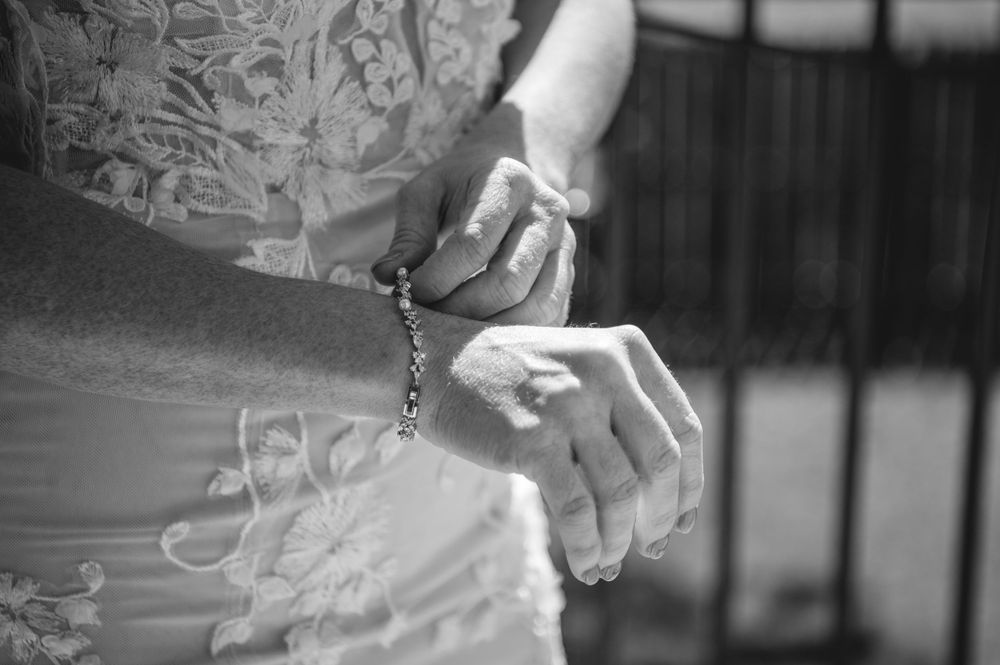Black and white photo of bride holding rosary beads with clasped hands in lace wedding dress.