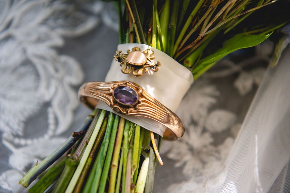Gold wedding rings with purple gemstone and floral detail resting on a green floral bouquet.