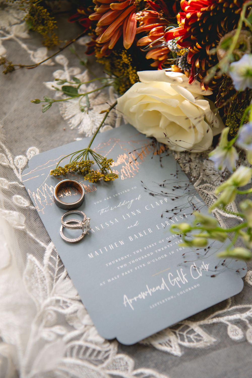 Dusty blue wedding invitation with rose gold script, gold rings, and autumn floral arrangement at Arrowhead Golf Club, Colorado.
