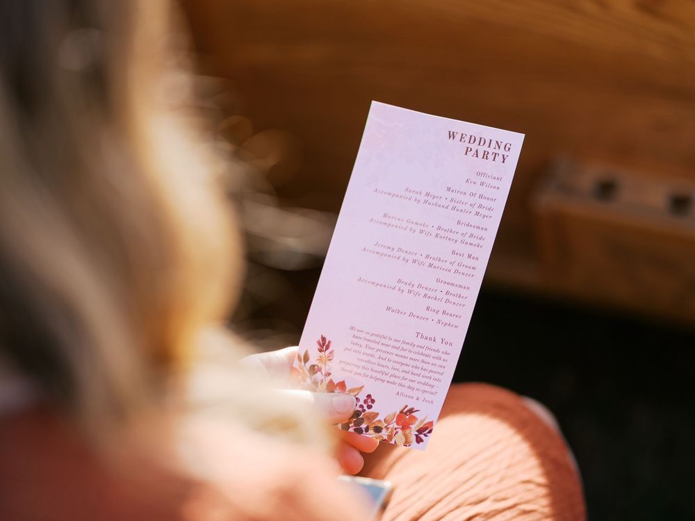 Woman holding a floral wedding party program card at a ceremony.