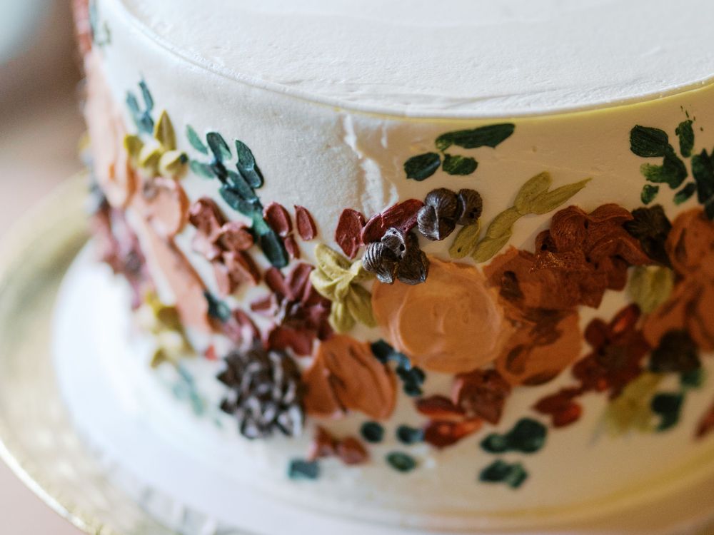 White wedding cake with hand-painted floral design featuring autumn blooms in rust, brown, and green tones.