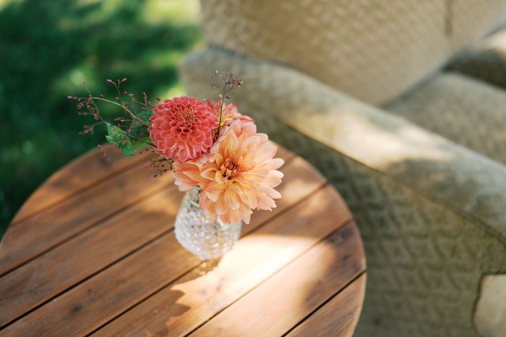 Crystal vase with pink and peach dahlias on a wooden table outdoors in soft sunlight.