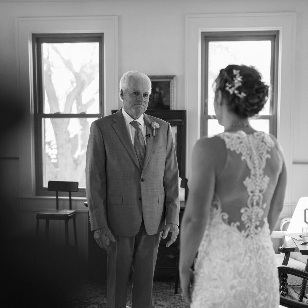 Black and white photo of a father seeing his daughter in her lace wedding dress for the first time.