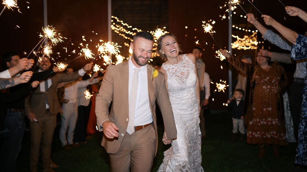 Bride and groom exit through sparkler tunnel during romantic nighttime wedding send-off celebration.