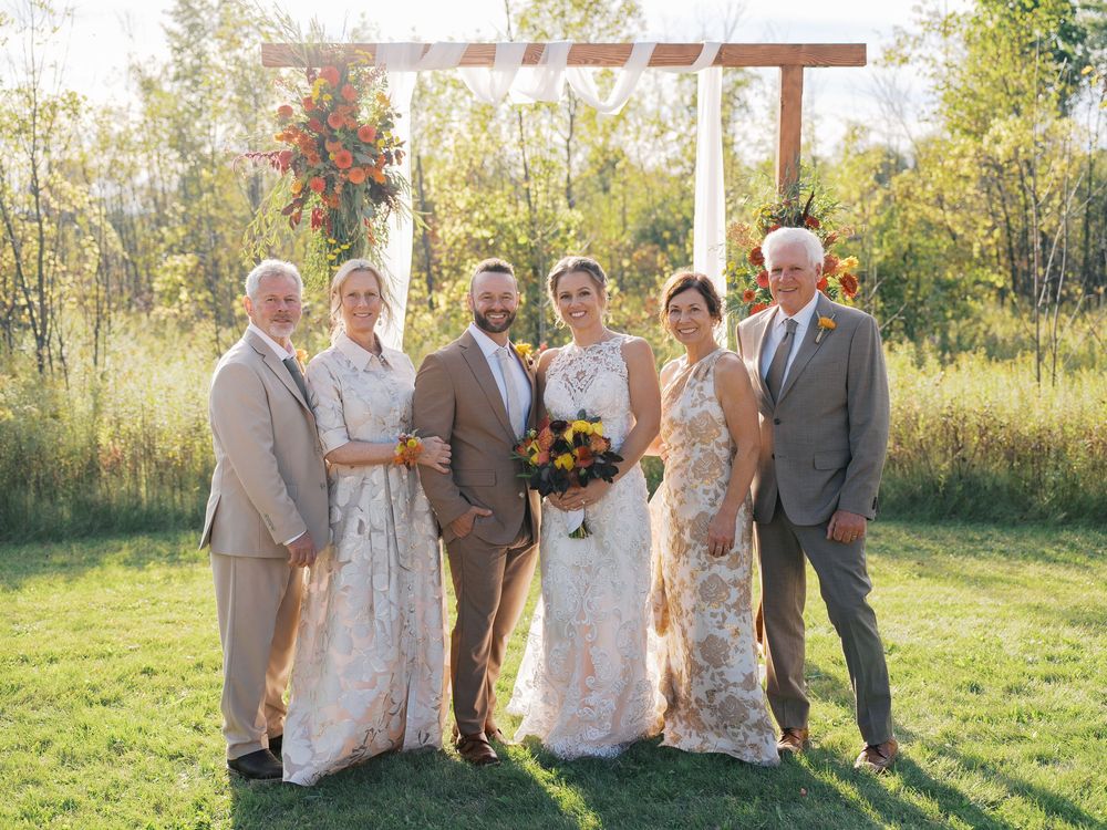 Wedding party of six posing outdoors in front of rustic wooden arch with colorful fall flowers.