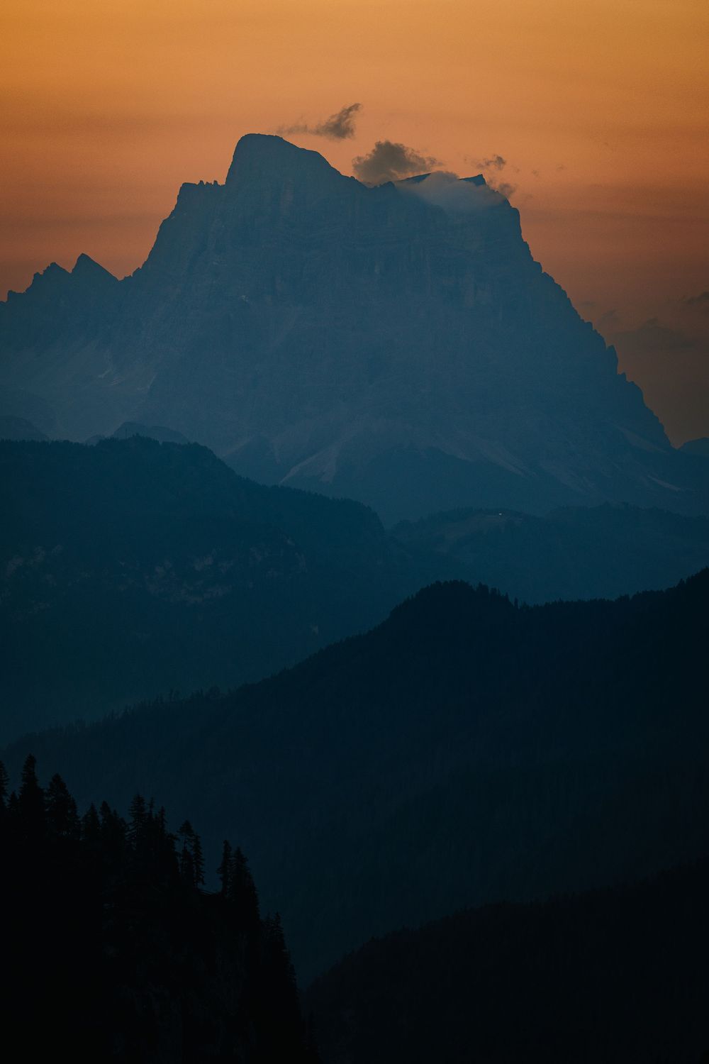 Dark blue Dolomites peak silhouetted against an orange sunrise sky above layered ridges and forest, Italy. Photo: Jan Virt