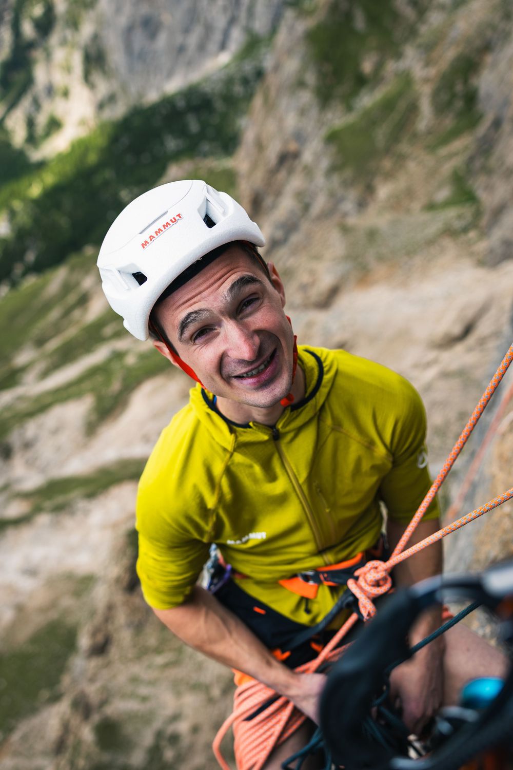 Smiling Adam Ondra in a yellow top and white helmet looks up from the belay on Egoland, Marmolada. Photo: Jan Virt