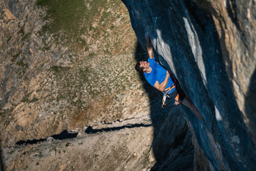 Adam Ondra in a blue top climbing the steep orange and grey limestone of Egoland, Marmolada South Face, Dolomites. Photo: Jan Virt