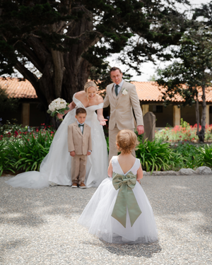 Bride and groom pose with flower girl and ring bearer at outdoor wedding ceremony with lush garden backdrop.