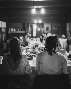 Black and white photo of bride and groom seated at head table during indoor wedding reception dinner.