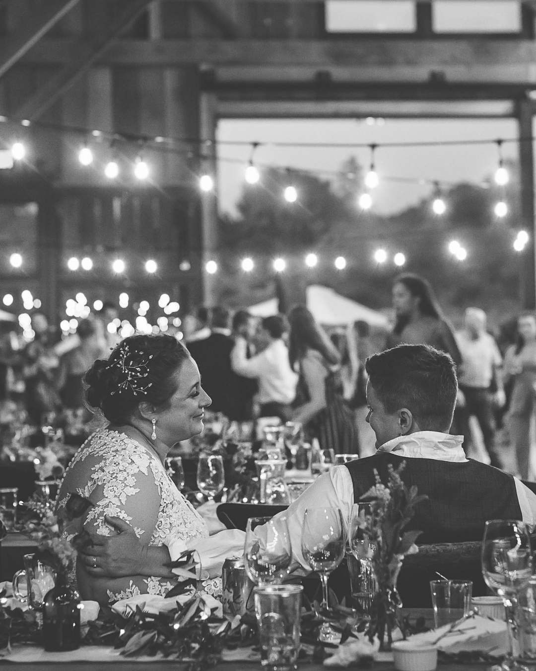Black and white photo of a bride and groom sharing a moment at their elegant wedding reception with string lights.