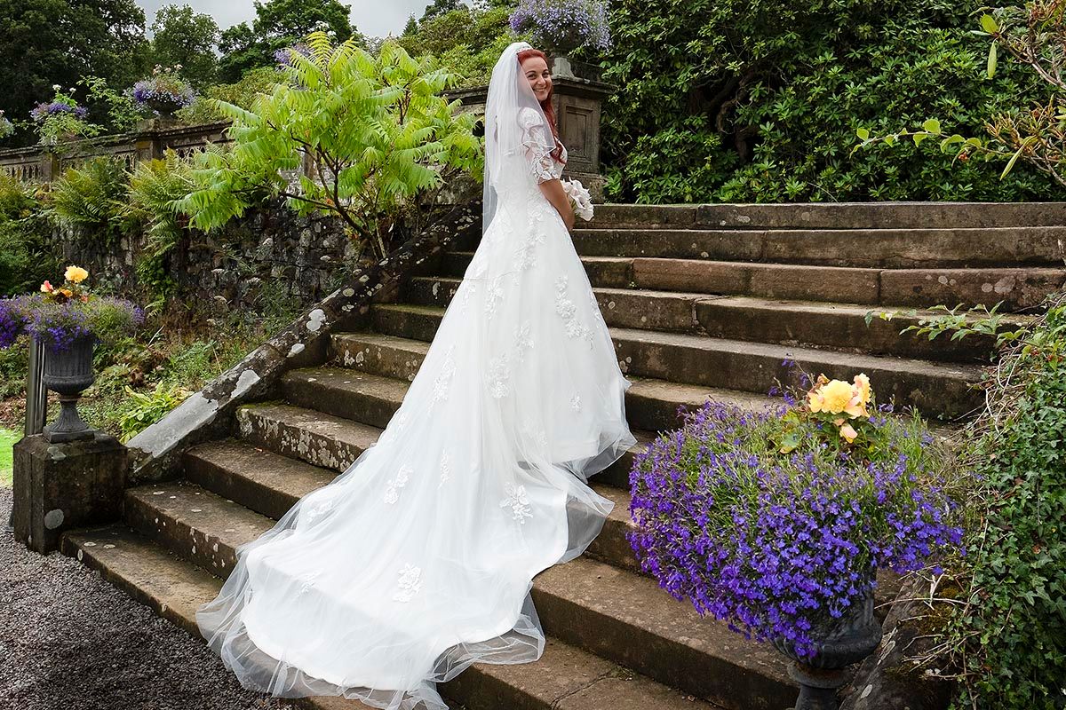 Bride posing in her lace wedding dress in the gardens at Auchen Castle