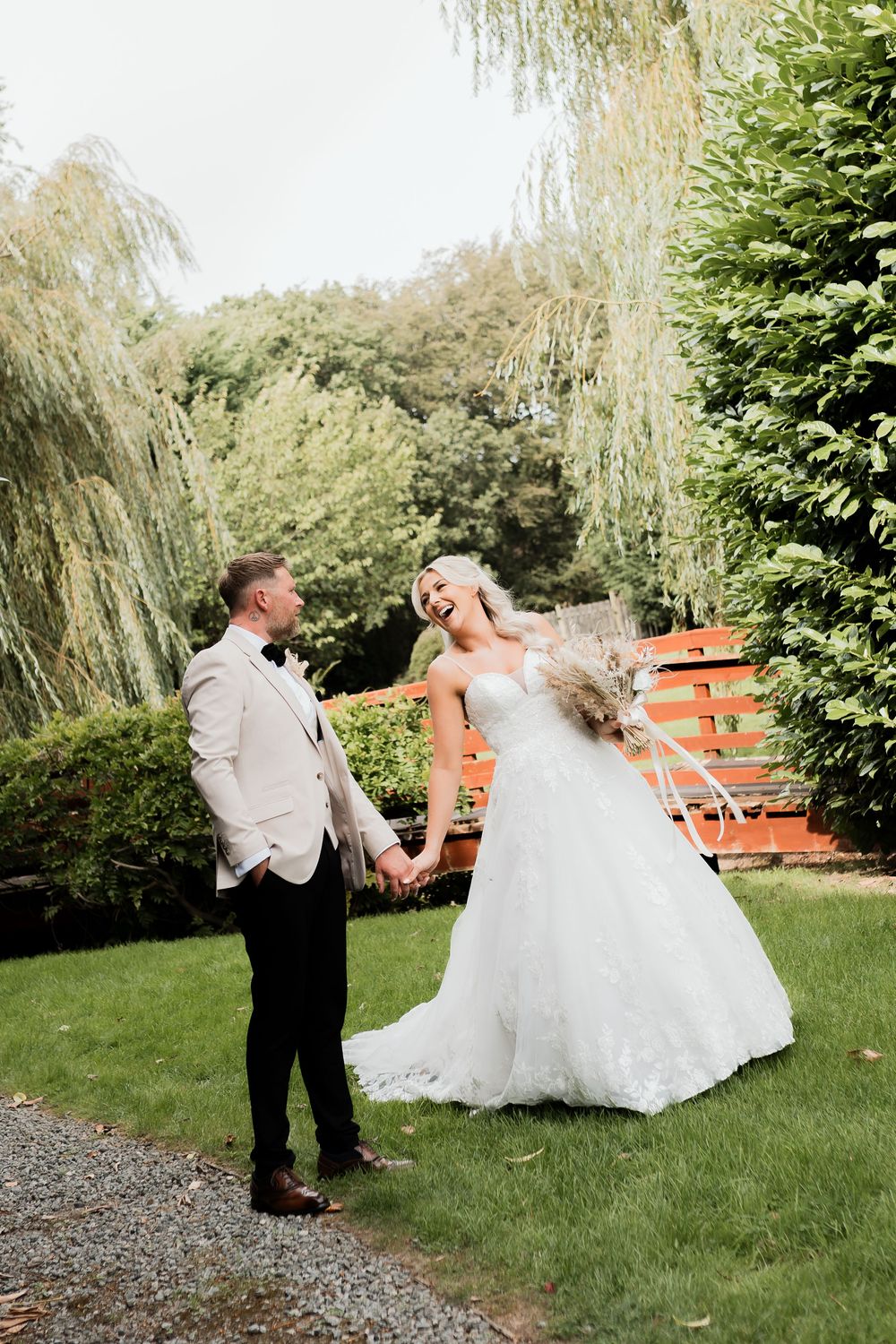 A joyful bride and groom hold hands and laugh together in a lush garden on their wedding day.