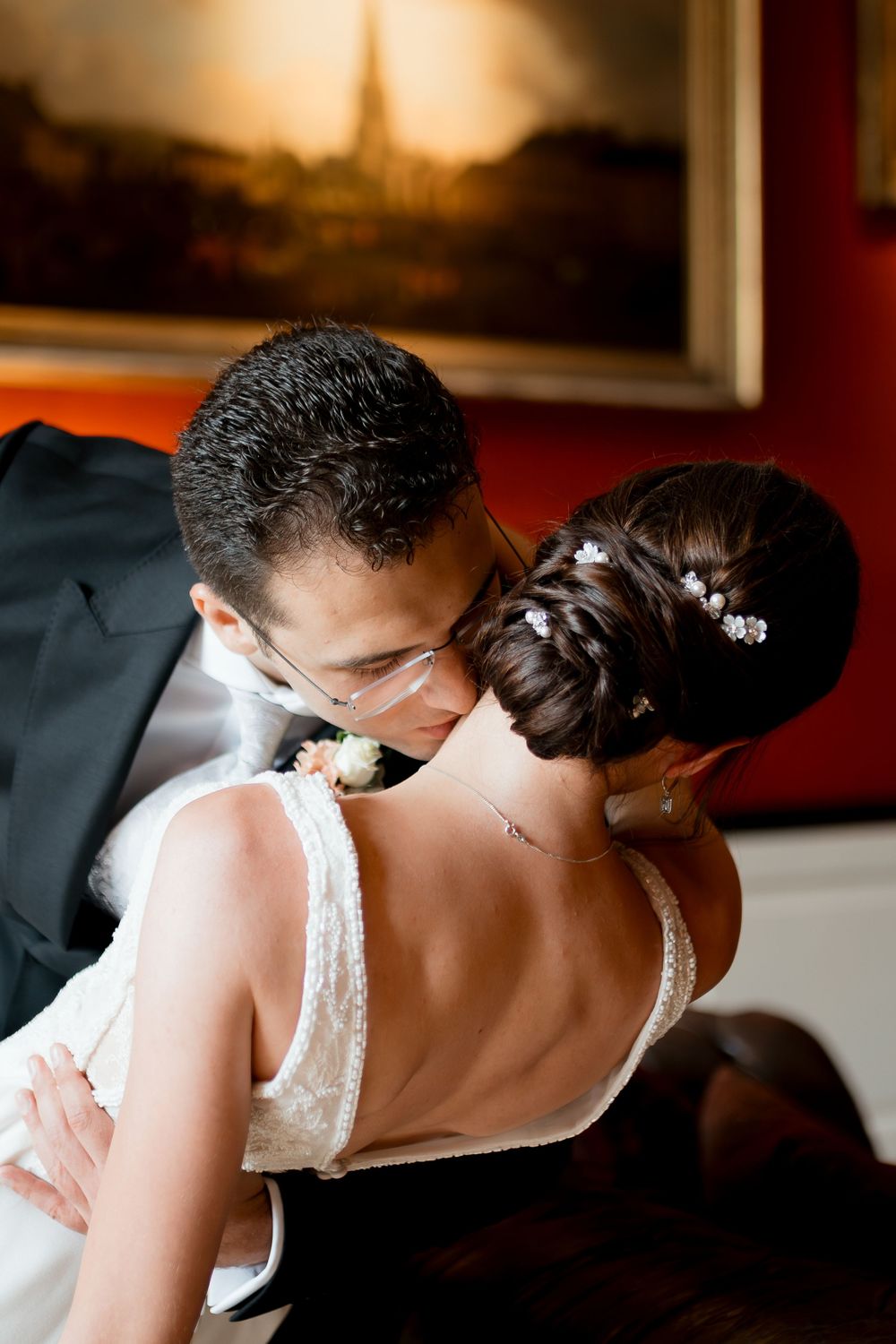 Groom in black suit kissing bride in white lace dress with elegant updo hairstyle at wedding reception.