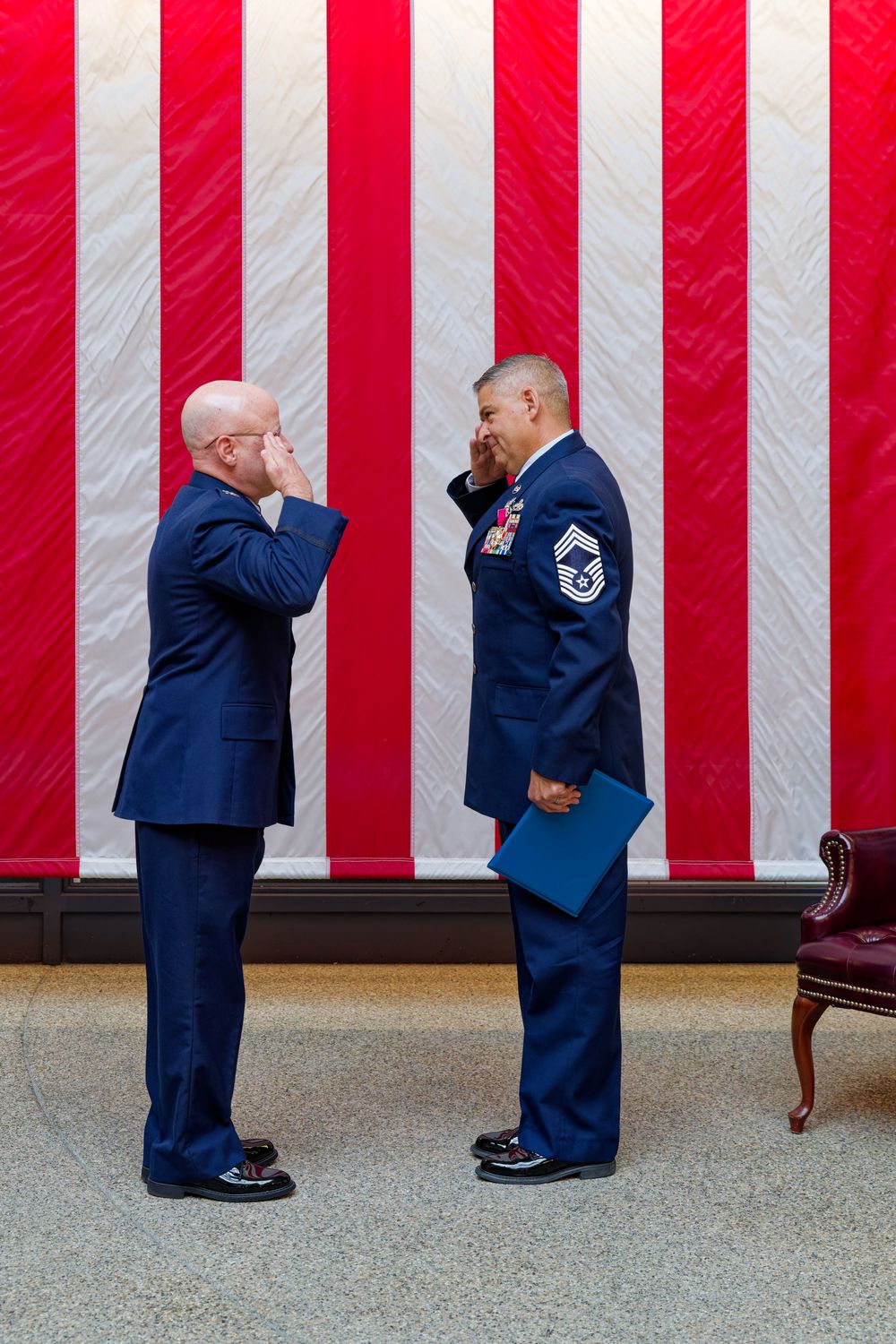 Two Air Force officers exchange salutes in front of an American flag at a retirement ceremony.