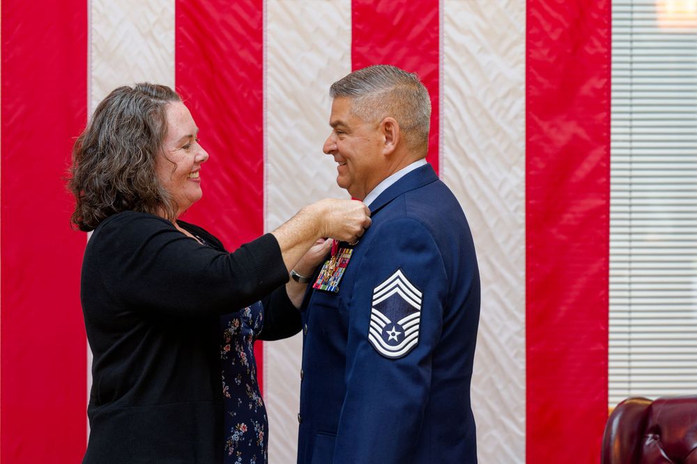 Woman pins a medal on a senior Air Force master sergeant uniform during a military promotion ceremony.