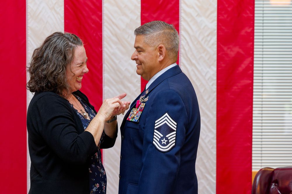 Woman smiles while pinning medals on a decorated Air Force senior NCO at a military ceremony.