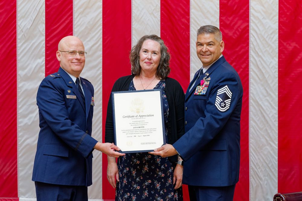 Two Air Force officers present a framed certificate to a woman during a military recognition ceremony.