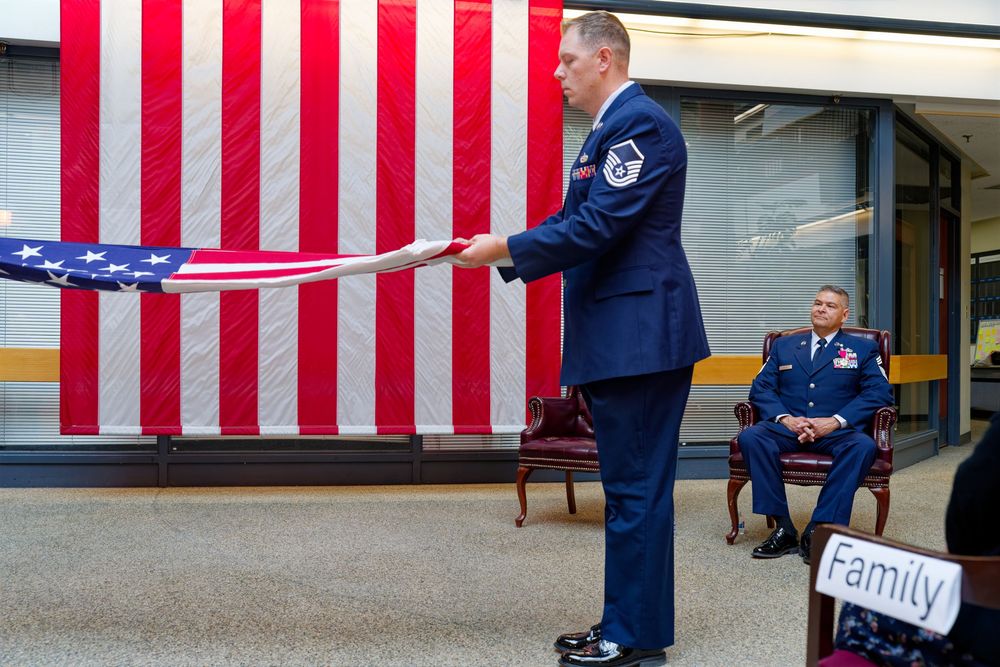 Air Force officer carefully folds an American flag during a formal military retirement ceremony indoors.