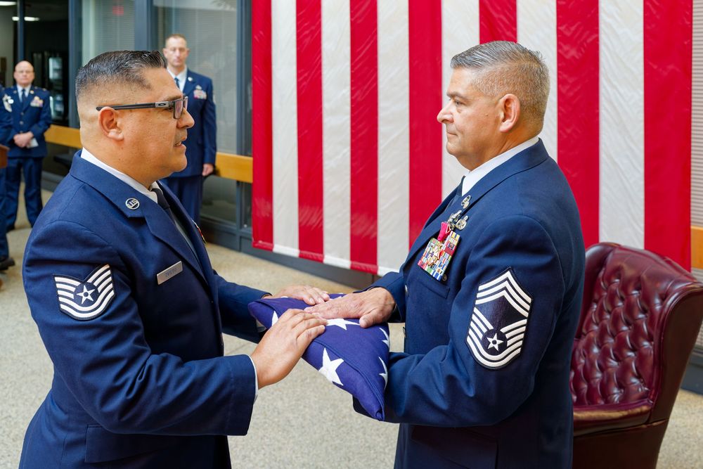 Air Force senior master sergeant receives a folded American flag from a fellow serviceman at a ceremony.