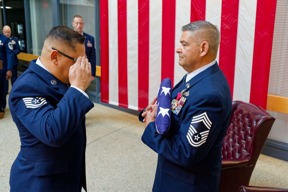 Air Force serviceman salutes a senior master sergeant holding a folded American flag at a ceremony.
